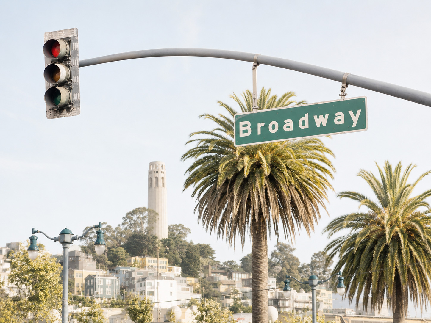 A Broadway street sign with palm trees and Coit Tower in the background