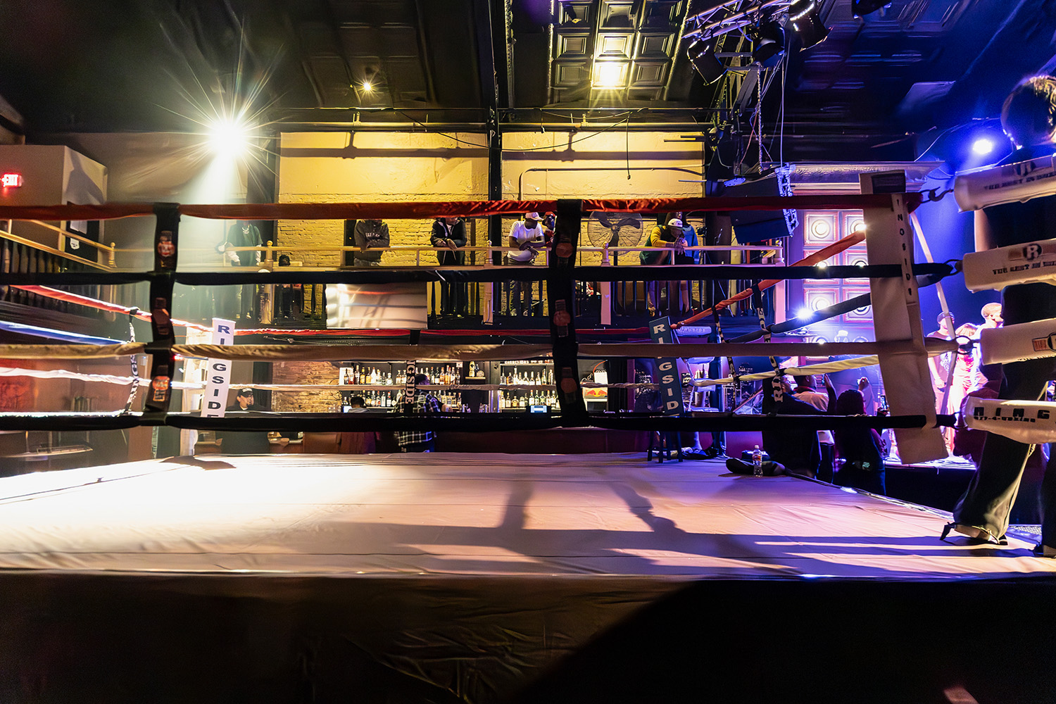 Ringside view of the boxing ring with the Broadway Studios balcony and event lighting behind it